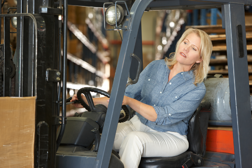 woman-driving-fork-lift-truck-in-warehouse-PFNLDSJ